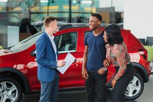 happy african couple choosing luxury car at vehicle dealership looking at the interior photo