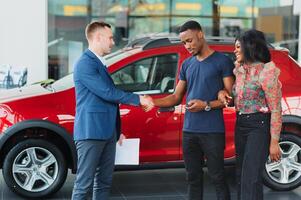 vendedor demostración nuevo coche a africano Pareja en sala de exposición foto