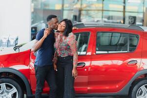 Smiling African American couple hugging and smiling at camera at new car showroom photo