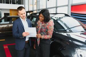 Woman buying the car. Lady in a car salon. Elegant black girl photo