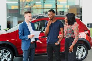 happy african couple choosing luxury car at vehicle dealership looking at the interior photo