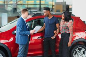 vendedor demostración nuevo coche a africano Pareja en sala de exposición foto