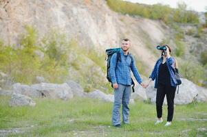 Couple enjoying beautiful views on the mountains, while traveling with backpacks in the mountains during the summer vacations photo