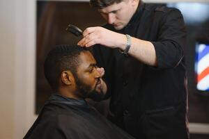 negro hombre en el peluquería. linda negro hombre hace un Corte de pelo en el africano salón. pelo estilo. Corte de pelo para adultos foto