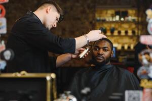 Portrait of young black man being trimmed with professional electric clipper machine in barbershop.Male beauty treatment concept. Young African guy getting new haircut in barber salon photo