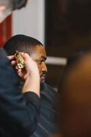 Portrait of young black man being trimmed with professional electric clipper machine in barbershop.Male beauty treatment concept. Young African guy getting new haircut in barber salon photo