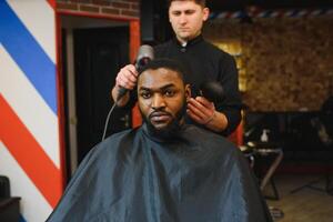 de cerca de proceso de guarnición de pelo en Barbero tienda. calificado Barbero acuerdo clíper en manos y de corrección forma de pelo a masculino cliente sentado en silla. concepto de Corte de pelo y afeitado. foto