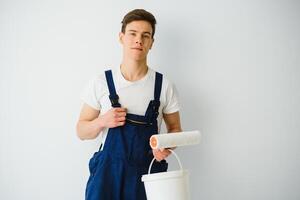 young man in blue overalls painting wall into white color with a roller photo