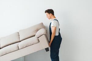 Loader moves sofa, couch. worker in overalls lifts up sofa, white background. Delivery service concept. Courier delivers furniture in case of move out, relocation. photo