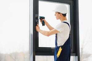 Workman in overalls installing or adjusting plastic windows in the living room at home photo