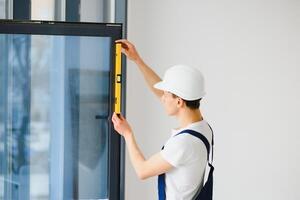 Workman in overalls installing or adjusting plastic windows in the living room at home photo