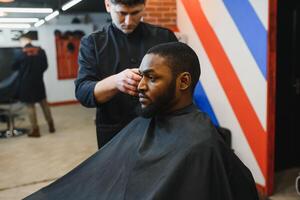 African male client getting haircut at barber shop from professional hairstylist. photo