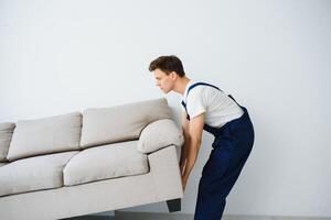 Loader moves sofa, couch. worker in overalls lifts up sofa, white background. Delivery service concept. Courier delivers furniture in case of move out, relocation. photo