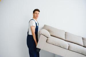 Loader moves sofa, couch. worker in overalls lifts up sofa, white background. Delivery service concept. Courier delivers furniture in case of move out, relocation. photo