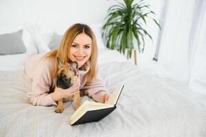 Young woman with dog and book relaxing indoors at home, reading. photo