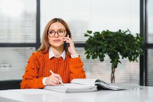 Portrait of happy lady typing in mobile while locating at desk in office photo