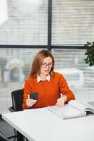 Portrait of happy lady typing in mobile while locating at desk in office photo