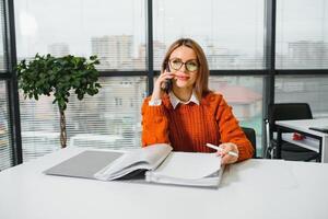 Portrait of happy lady typing in mobile while locating at desk in office photo