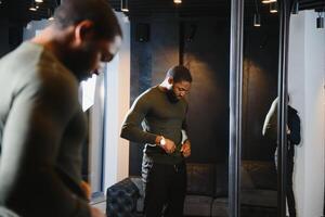 Stylish casual african american man at fitting room clothes store, looking on mirror. The concept of stylish men's clothing. photo