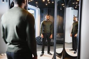 Stylish casual african american man at fitting room clothes store, looking on mirror. The concept of stylish men's clothing. photo