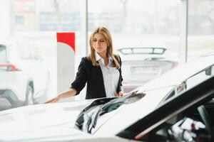 Young beautiful woman showing her love to a car in a car showroom. photo