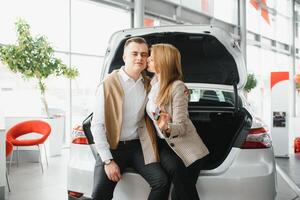 Happy young couple chooses and buying a new car for the family in the dealership photo