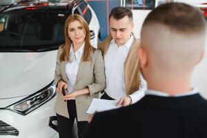 mature salesman showing new car to a couple in showroom. photo