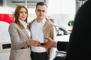 Happy young couple chooses and buying a new car for the family in the dealership photo