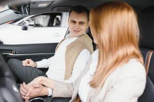 Happy young couple chooses and buying a new car for the family in the dealership photo