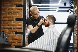 Making haircut look perfect. Young bearded man getting haircut by hairdresser while sitting in chair at barbershop. photo