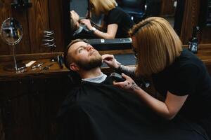 Barbershop or hairdresser concept. Woman hairdresser cuts beard with scissors. Man with long beard, mustache and stylish hair. Guy with modern hairstyle visiting hairdresser photo