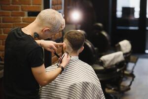 Making haircut look perfect. Young bearded man getting haircut by hairdresser while sitting in chair at barbershop. photo