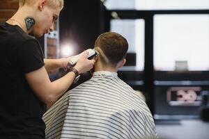 Making haircut look perfect. Young bearded man getting haircut by hairdresser while sitting in chair at barbershop. photo