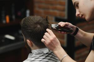 Making haircut look perfect. Young bearded man getting haircut by hairdresser while sitting in chair at barbershop. photo