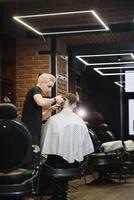 Young handsome barber making haircut of attractive bearded man in barbershop. photo