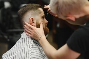 Young handsome barber making haircut of attractive bearded man in barbershop. photo