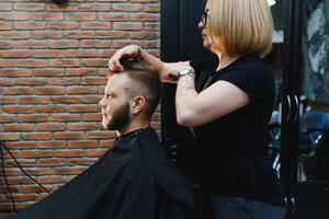 Woman barber cutting hair to a bearded man photo