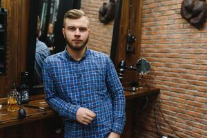 Perfection. Handsome bearded man at barbershop. Portrait of stylish young guy in jacket touching his hair while visiting barbershop or salon. Mens haircut. Barbershop concept. photo