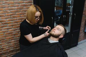 Barbershop or hairdresser concept. Woman hairdresser cuts beard with scissors. Man with long beard, mustache and stylish hair. Guy with modern hairstyle visiting hairdresser photo