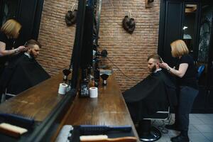 Stylish man sitting barber shop Hairstylist Hairdresser Woman cutting his hair Portrait handsome happy young bearded caucasian guy getting trendy haircut Attractive barber girl working serving client. photo