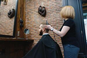 Stylish man sitting barber shop Hairstylist Hairdresser Woman cutting his hair Portrait handsome happy young bearded caucasian guy getting trendy haircut Attractive barber girl working serving client. photo