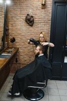 profesional peluquero mujer haciendo peinado de hermoso chico con eléctrico pelo clíper a Barbero tienda. foto