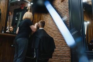 Stylish man sitting barber shop Hairstylist Hairdresser Woman cutting his hair Portrait handsome happy young bearded caucasian guy getting trendy haircut Attractive barber girl working serving client. photo