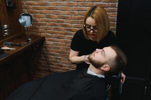 Barbershop or hairdresser concept. Woman hairdresser cuts beard with scissors. Man with long beard, mustache and stylish hair. Guy with modern hairstyle visiting hairdresser photo