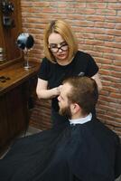 servicio cliente en peluquería. profesional Barbero chica, hembra peluquero haciendo moderno Corte de pelo para un hombre sentado en Barbero tienda silla. atención en un muchacha. peluquería, afeitado, guarnición, aseo. foto