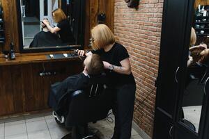 barbería o peluquero concepto. mujer peluquero cortes barba con tijeras. hombre con largo barba, Bigote y elegante cabello. chico con moderno peinado visitando peluquero foto