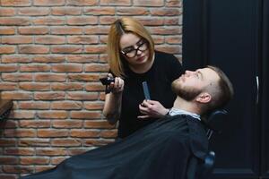 Barbershop or hairdresser concept. Woman hairdresser cuts beard with scissors. Man with long beard, mustache and stylish hair. Guy with modern hairstyle visiting hairdresser photo