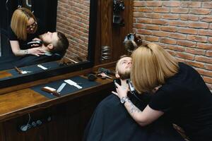 Barbershop or hairdresser concept. Woman hairdresser cuts beard with scissors. Man with long beard, mustache and stylish hair. Guy with modern hairstyle visiting hairdresser photo