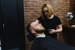 Barbershop or hairdresser concept. Woman hairdresser cuts beard with scissors. Man with long beard, mustache and stylish hair. Guy with modern hairstyle visiting hairdresser photo