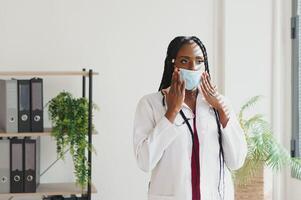 medicine, profession and healthcare concept - african american female doctor or scientist in protective facial mask in clinic. photo